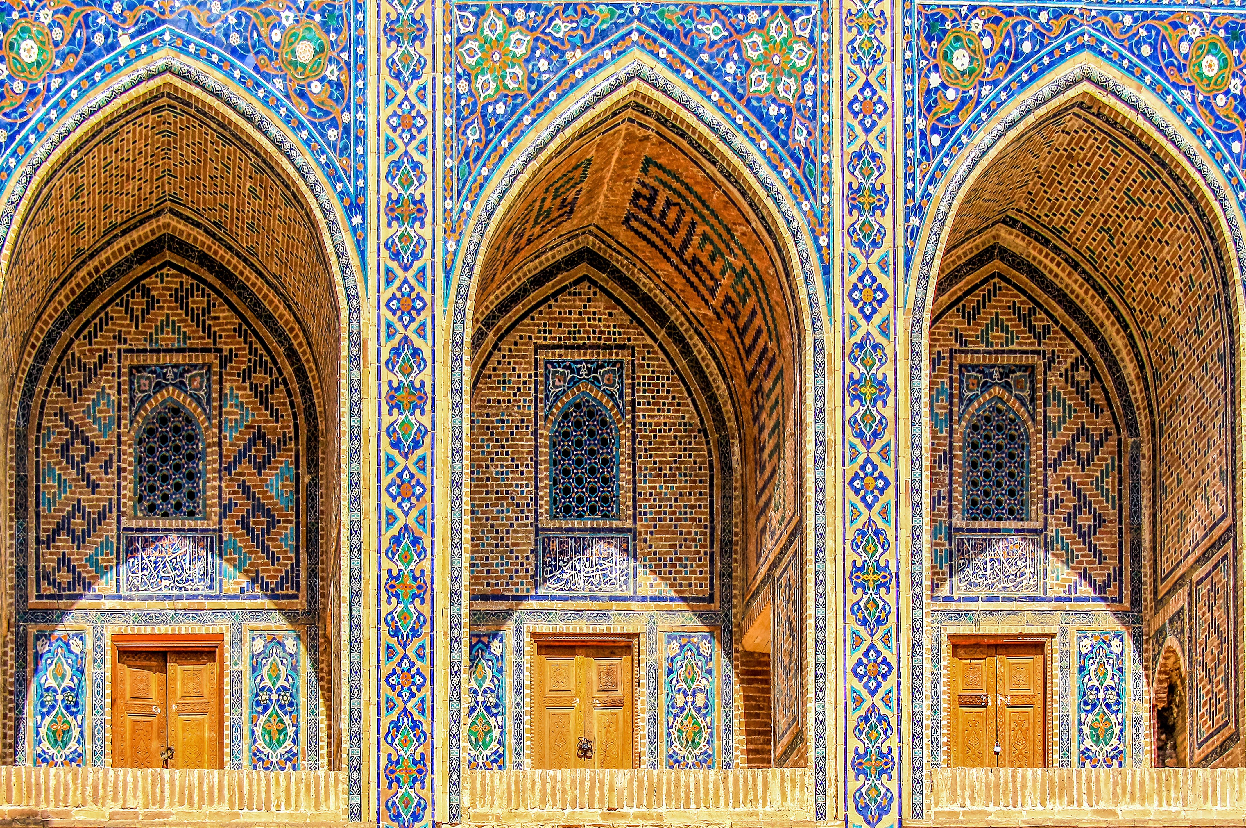 Sherdor Madrassah facade with blue, yellow and green tiles, wall with tall arches and windows