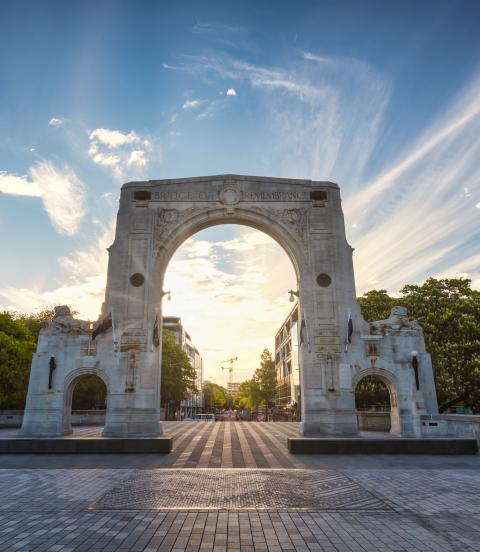 Sunset Panorama of the famous Bridge of Remembrance in Christchurch with New Zealand Flag blowing in the wind. Arch backlit against the sunset Sun