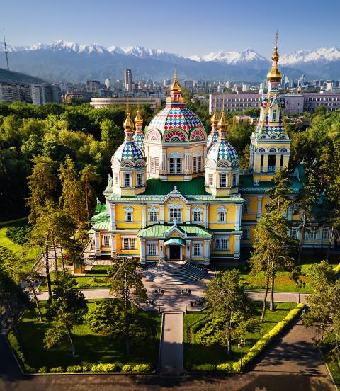 Aerial view of the Zenkov Cathedral in Panfilov Park against blue sky and and snowy mountains in Almaty city, Kazakhstan