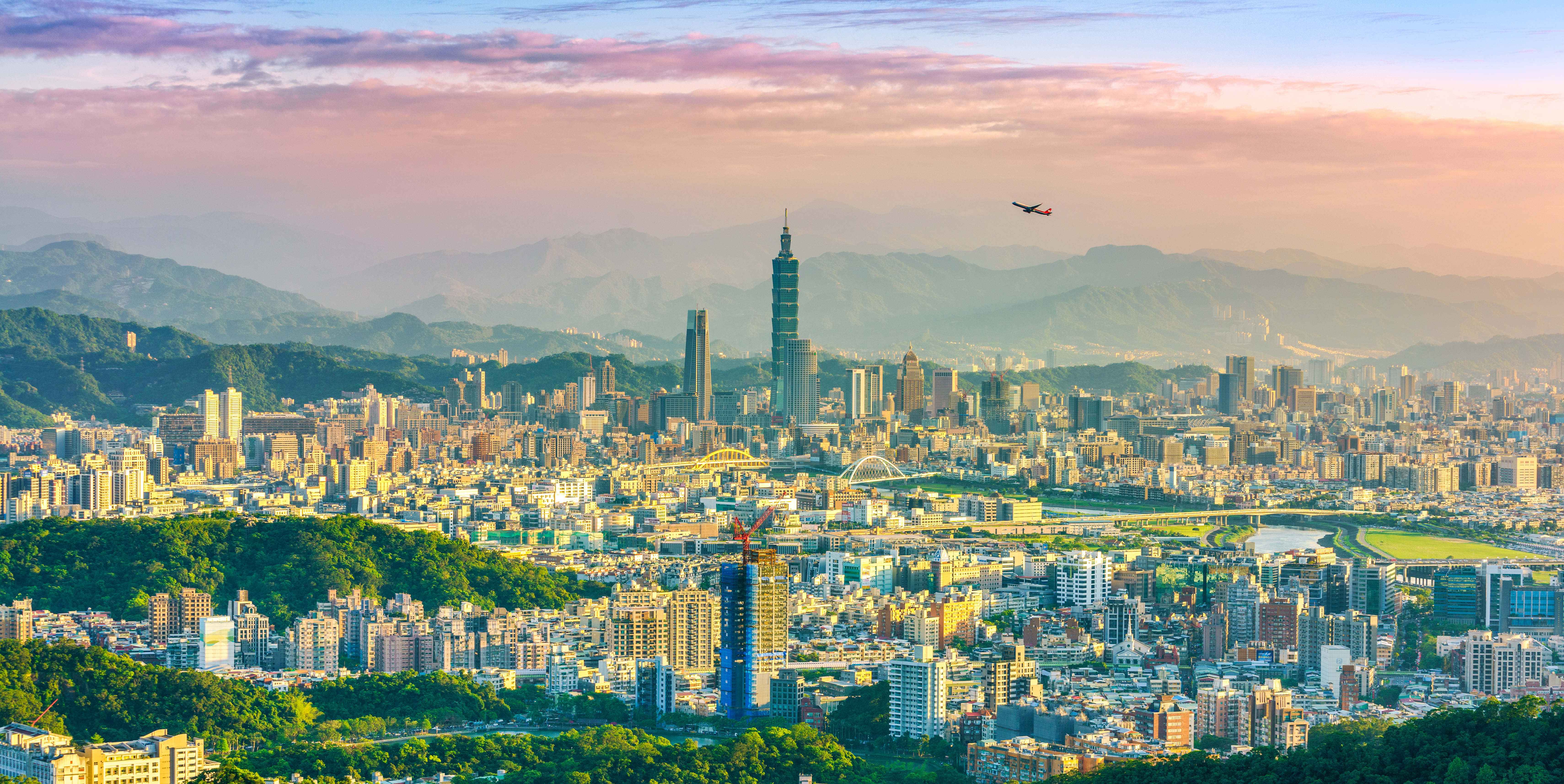 Airplane flying over Taipei city at sunset with mountains in the background