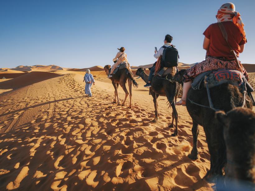 a caravan of camel rides passing through the Sahara Desert in Morocco